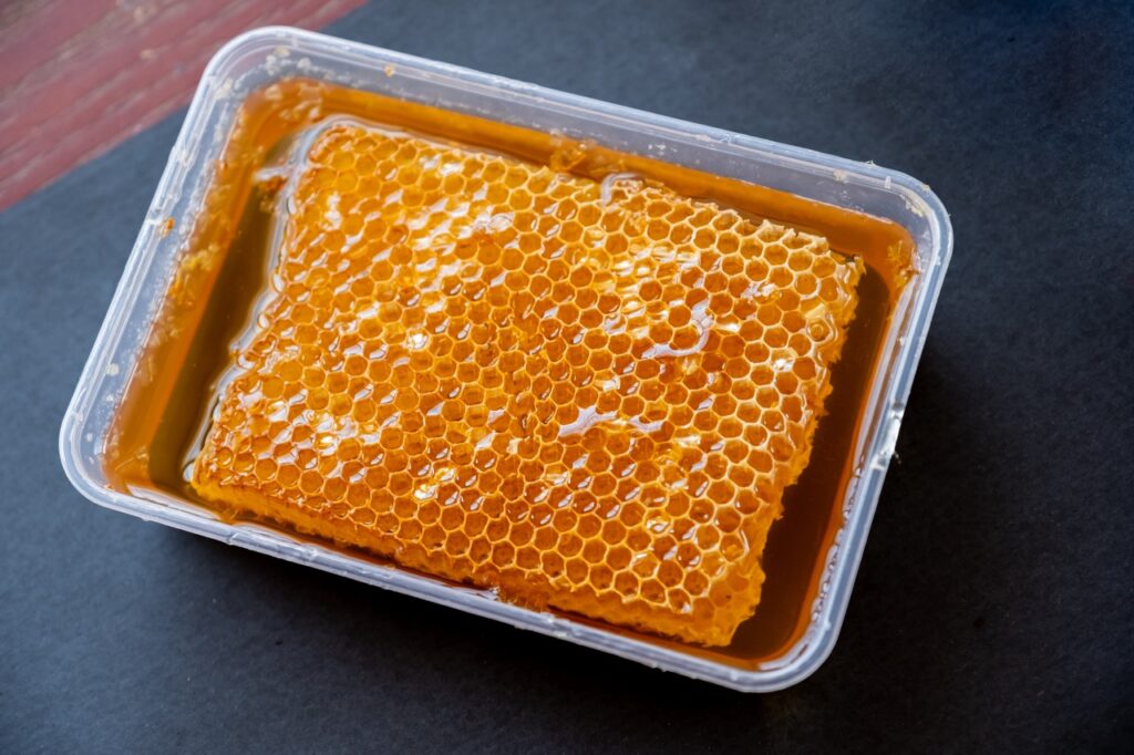 rauwe honingraat met vloeibare honing in een plastic bakje van BeeHome imker in Torhout